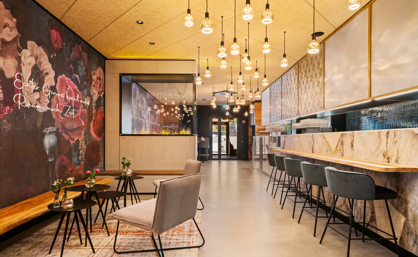 Reference image of the Hotel Lukullum in Friedrichshafen, dining and lounge area with a bar and a variety of floating light fittings