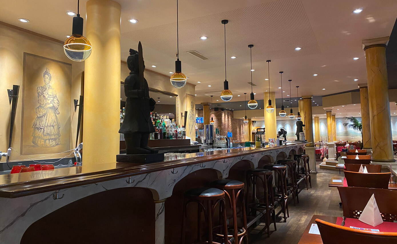 Reference image of Restaurant Han in Zug, showing blue and yellow light bulbs suspended above a bar