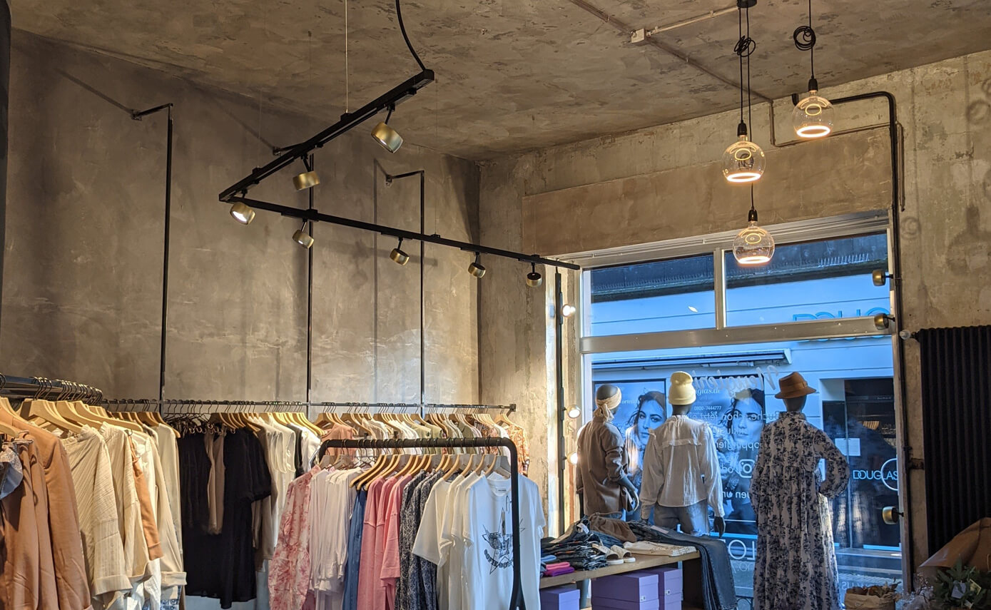 Reference image from Scola Raumkonzepte in Andernach: a clothes shop with a shop window and floating light fittings